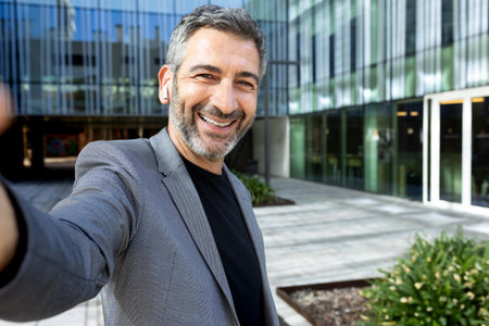 Selfie of mature caucasian businessman in the city near office buildings looking at camera smiling.Copy space.の写真素材