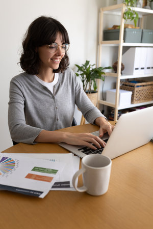 Caucasian woman working at home office. Happy female entrepreneur using laptop. Vertical imageの写真素材