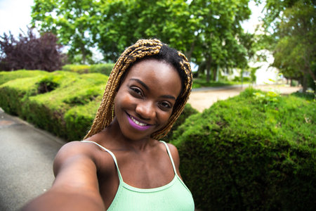 Happy African American female jogger taking selfie while running outdoors in the park looking at camera. Copy space.の写真素材
