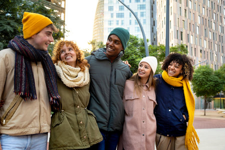 Group of happy multiracial friends laughing embracing together while walking around city on a winter...