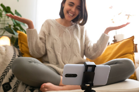 Young caucasian woman recording vlog at home with mobile phone. Female on a video call using phone. Selective focus.の写真素材