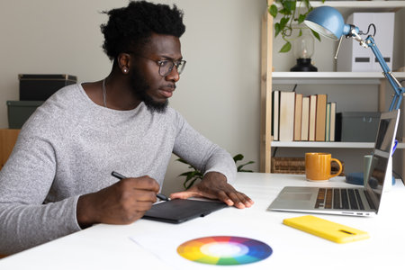 African American male graphic designer working at home using laptop and graphic tablet.の写真素材