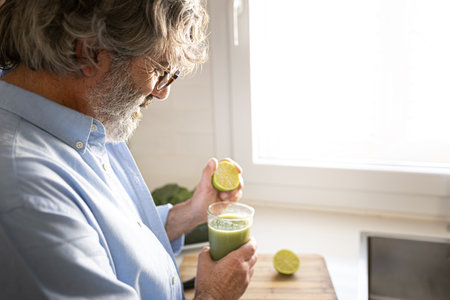 Mature man squeezing lime juice into green vegetable smoothie for breakfast. Copy space.の写真素材