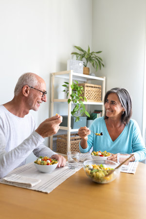 Mature married couple enjoying pasta salad for lunch. Couple looking at each other smiling while eating.の写真素材