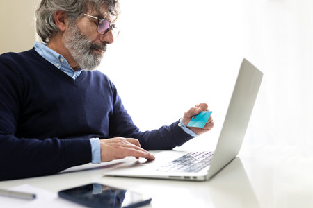 Senior businessman making online payment using laptop and credit cardの写真素材