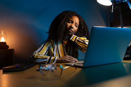 African American woman suffering from neck pain, working late at night using laptop.の写真素材