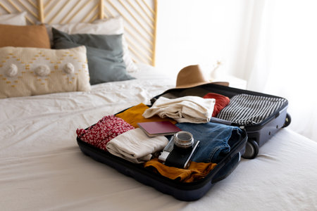 Open suitcase on the bed full of clothes and summer items: hat, sunglasses, swimsuit. Ready for vacations.の写真素材