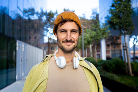Young man wearing headphones and beanie smiling in urban settingの写真素材
