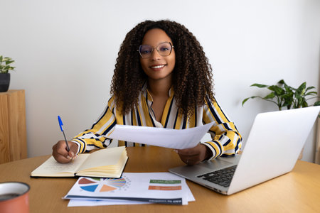 Happy busy African American woman working at home office looking at camera smiling.の写真素材