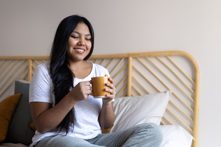 Young latin woman enjoying morning coffee in bedの写真素材