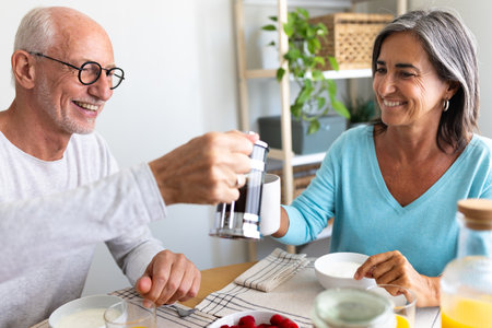 Happy mature couple having healthy breakfast together at home dining room. Man serving coffee to wife.の写真素材