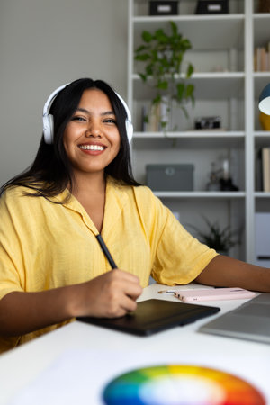 Latin graphic designer working from home using graphic tablet and headphonesの写真素材