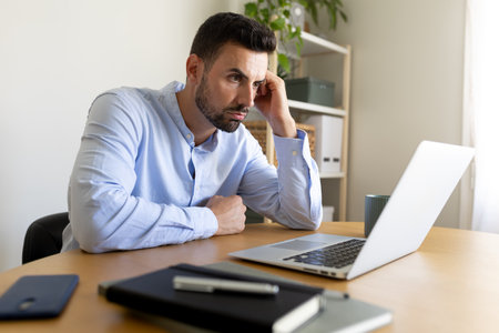 Man feeling exhausted and overworked looking at laptop at home office.の写真素材