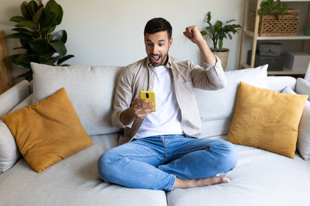 Young man using phone celebrating victory, successful achievement with fist up in the air. Arm raised.の写真素材