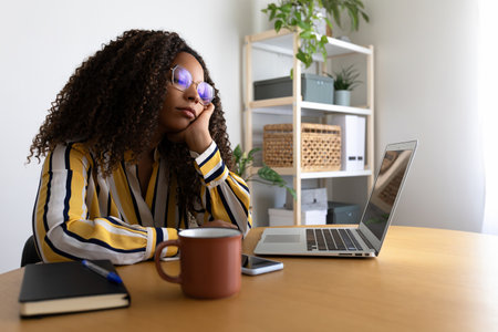 African American woman feeling bored and tired working using laptop at home office.の写真素材