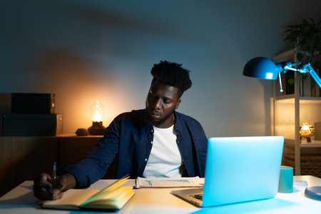Focused male employee working late at night on charts and laptop.の写真素材