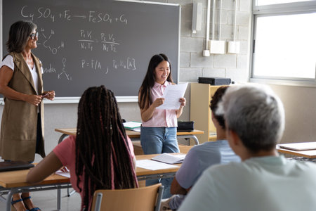 Smiling student presenting work in chemistry class with teacher and students watchingの写真素材