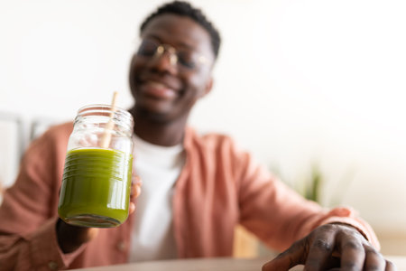 Smiling man holding green smoothie in glass jar with wooden strawの写真素材