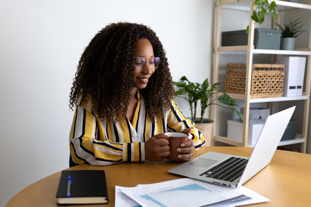 Black woman working at home office having coffee. African American female entrepreneur using laptop.の写真素材