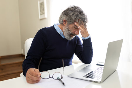 Tired mature entrepreneur suffering from headache while using laptop at homeの写真素材