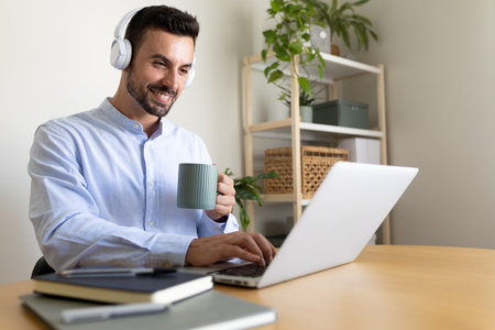 Caucasian man with headphones working at home office. Happy male entrepreneur using laptop.の写真素材