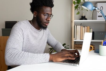 Black man working at home office using laptop. African American male college student studying at home.の写真素材