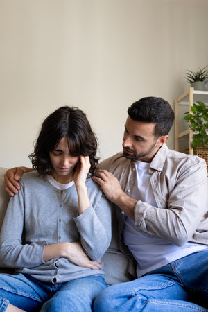 Front view of man consoling depressed woman sitting on the sofa at home living room. Vertical image.の写真素材