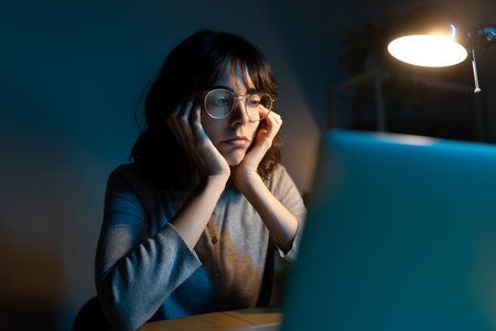 Bored woman working late at night using laptop at home office.の写真素材