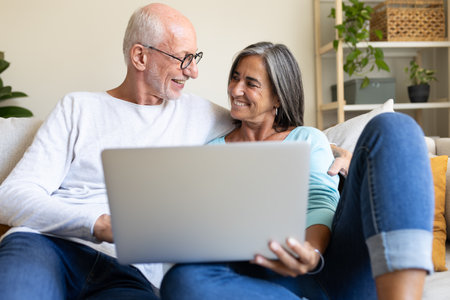 Happy mature married couple in love using laptop relaxing on the couch at home living room looking at each other.の写真素材
