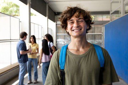 Smiling male student wearing backpack at school hallwayの写真素材