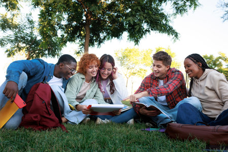 Happy multi-ethnic students studying together sitting on grass in a parkの写真素材