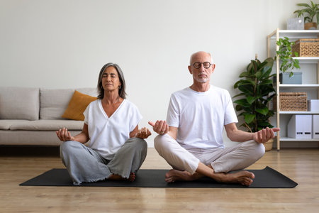 Front view of mature couple meditating at home living room sitting on a mat.の写真素材