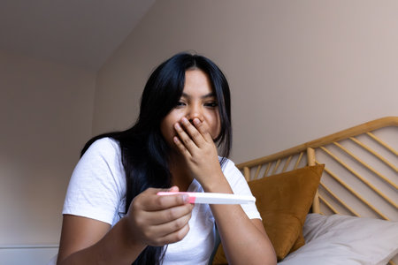 Young latina woman holding pregnancy test covering mouth with handの写真素材