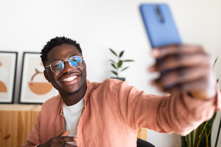 Cheerful young man taking selfie with smartphone at homeの写真素材