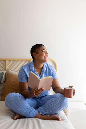 Serene woman enjoying morning coffee and book in bedの写真素材