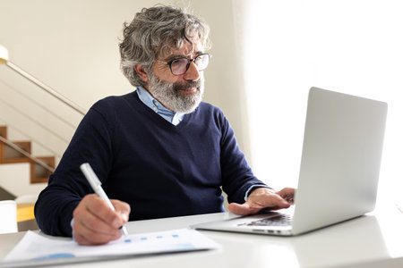 Mature business man working with laptop at home office taking notes.の写真素材