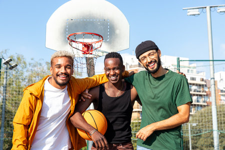 Happy multiracial friends embracing laughing and having fun standing in basketball court outdoors looking at camera.の写真素材