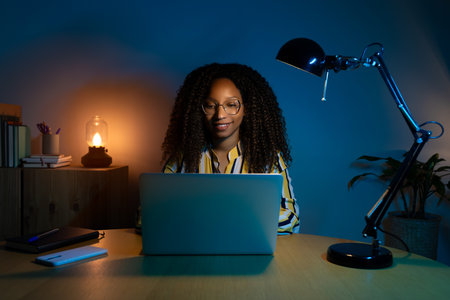 Front view of Black woman working late at night with laptop at home.の写真素材
