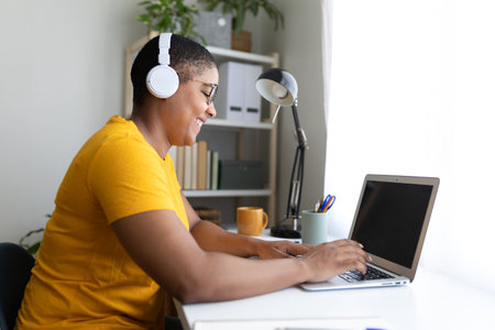 Smiling woman working from home using laptop listening music with headphonesの写真素材
