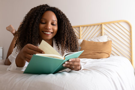 Happy Black woman reading a book in bed smiling. Copy spaceの写真素材