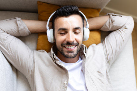 Top view of happy man relaxing at home, lying down on the couch listening to music with headphones.の写真素材