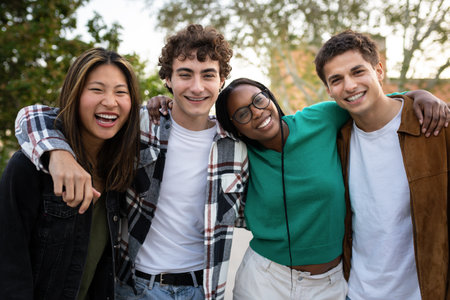 Happy multi-ethnic students embracing and smiling outdoors looking at cameraの写真素材