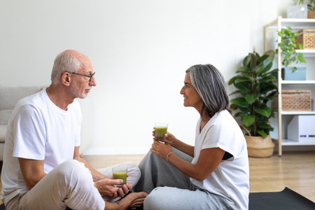 Mature woman drinking healthy green vegetable smoothie after exercising at home with husband.の写真素材