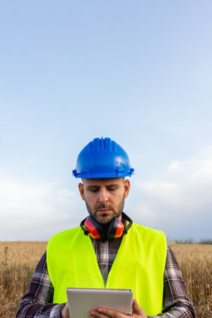 Agricultural engineer working with digital tablet in wheat field wearing safety equipmentの写真素材