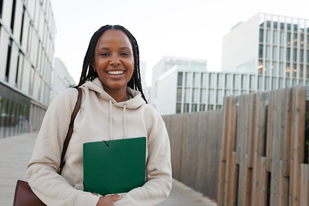 Smiling student holding green notebook outdoorsの写真素材