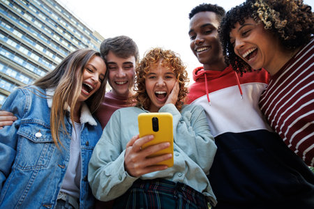 Group of excited students sharing a funny video on a smartphoneの写真素材