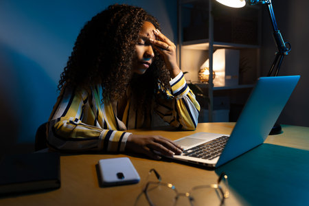 African American woman working late at night using laptop at home office having headache.の写真素材
