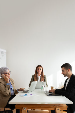 Mature woman talking on the phone at the office while coworkers working using laptop. Vertical...