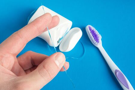 dental floss and toothbrush in hand on a blue background, the concept of care for the oral cavity, preventing tooth decayの写真素材