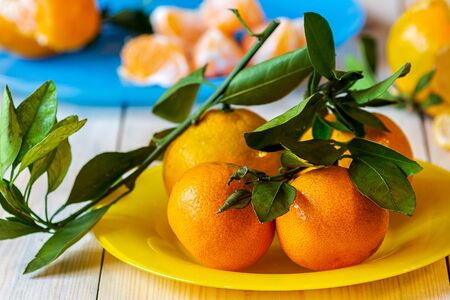 beautiful ripe tangerines with green leaves on bright yellow plateの写真素材